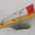 Wooden tip-up ice fishing rigs standing on a frozen snow-covered lake