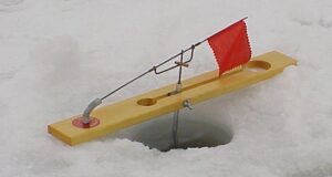 Wooden tip-up ice fishing rigs standing on a frozen snow-covered lake