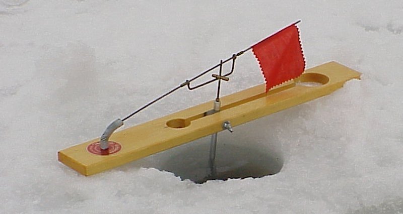 Wooden tip-up ice fishing rigs standing on a frozen snow-covered lake